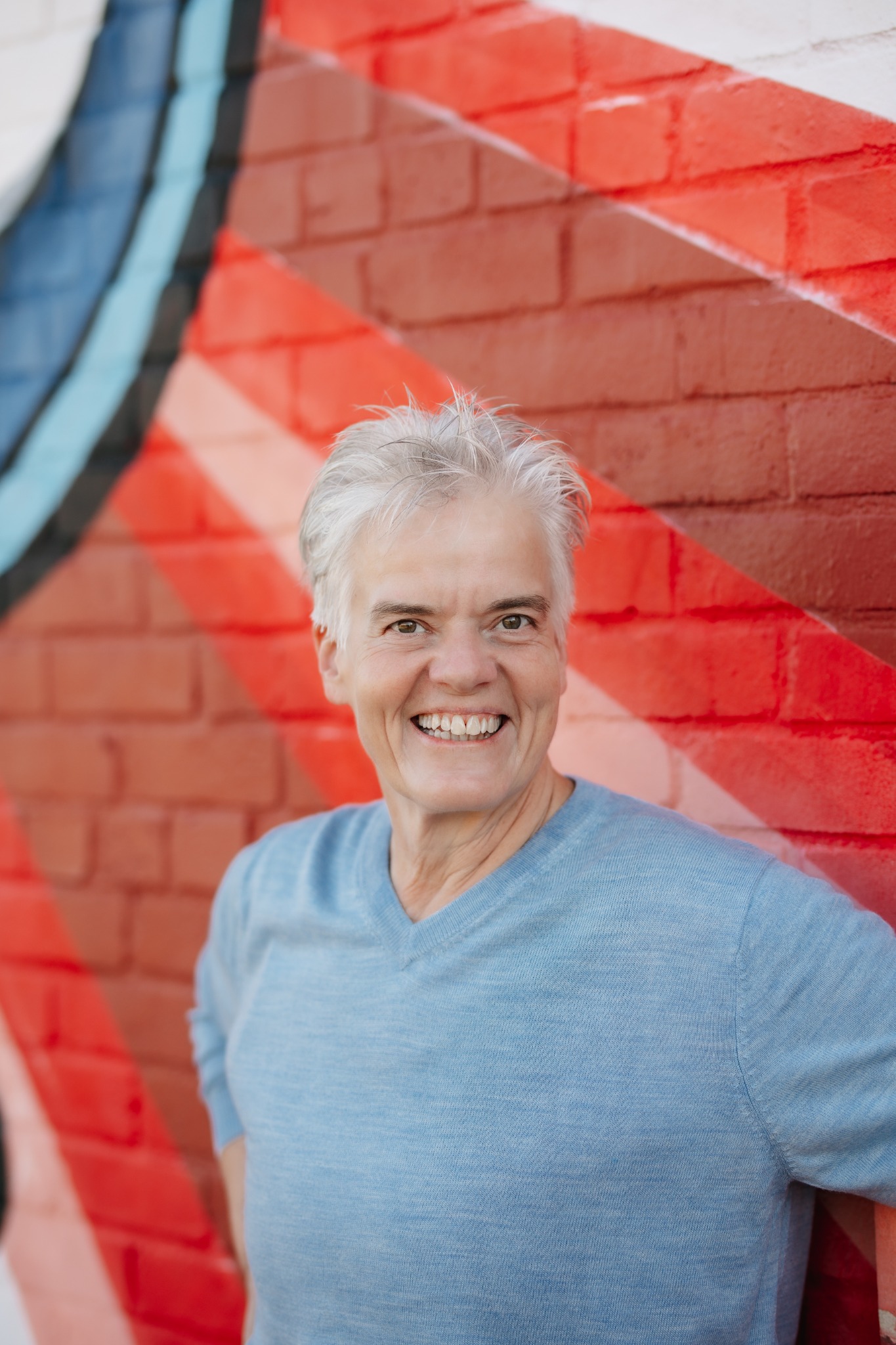 Deana Coble smiling in a blue shirt in front of a colorful mural