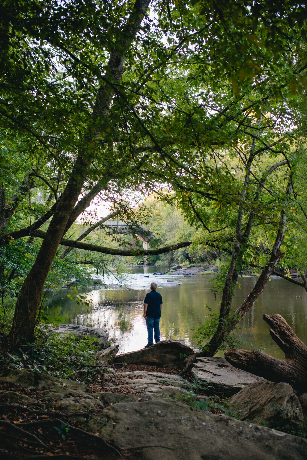 Deana standing beneath trees beside the river
